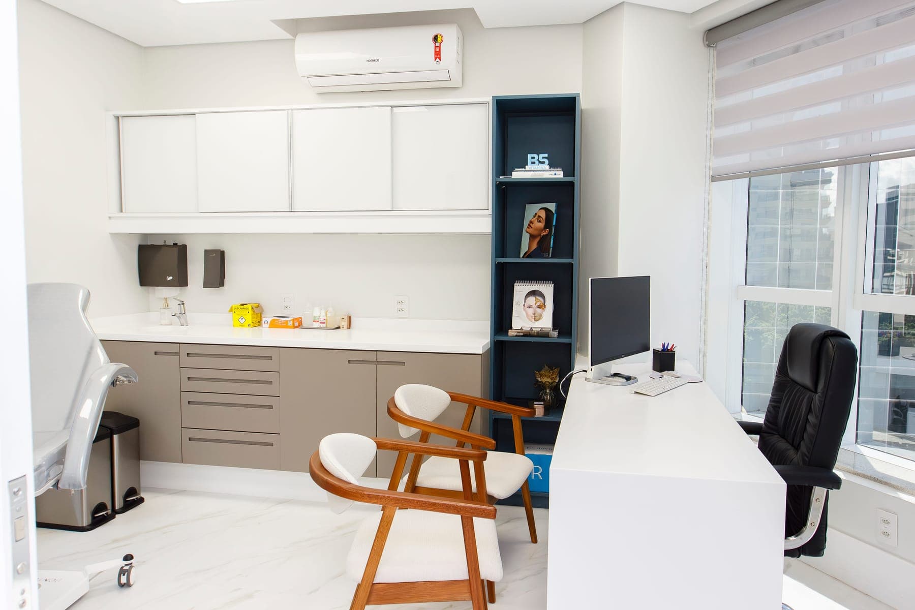 Sala de avaliação com escrivaninha, cadeiras e luz natural.